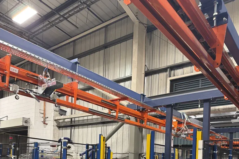 MCM Autotrack Kurven-Hängefördererabschnitt Close-up of curved orange MCM Autotrack overhead conveyor track within an automotive manufacturing facility